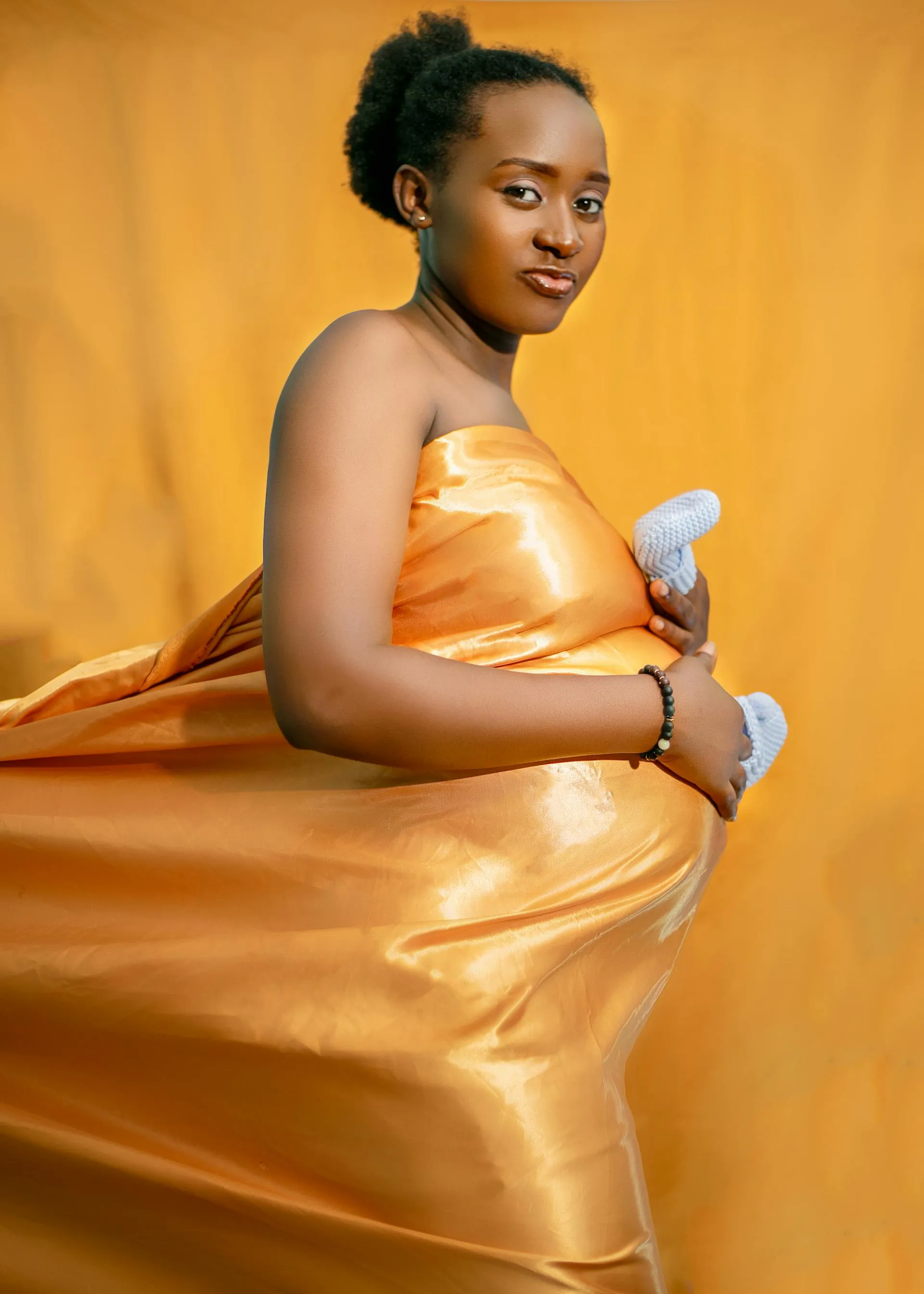 African mother-to-be in a flowing golden dress, gently cradling her belly